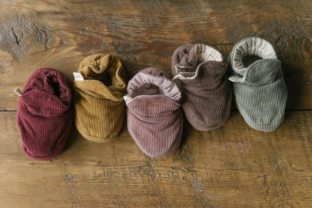 Corduroy baby booties, lined up on a wooden dresser.
