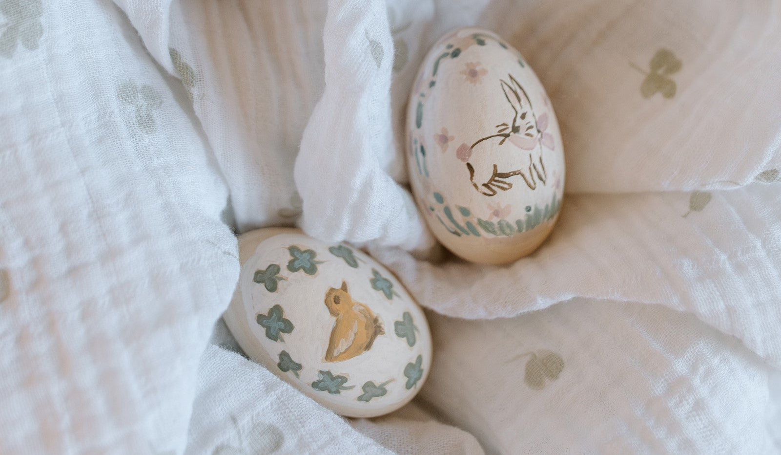 Two hand-painted eggs sit on a clover swaddle.