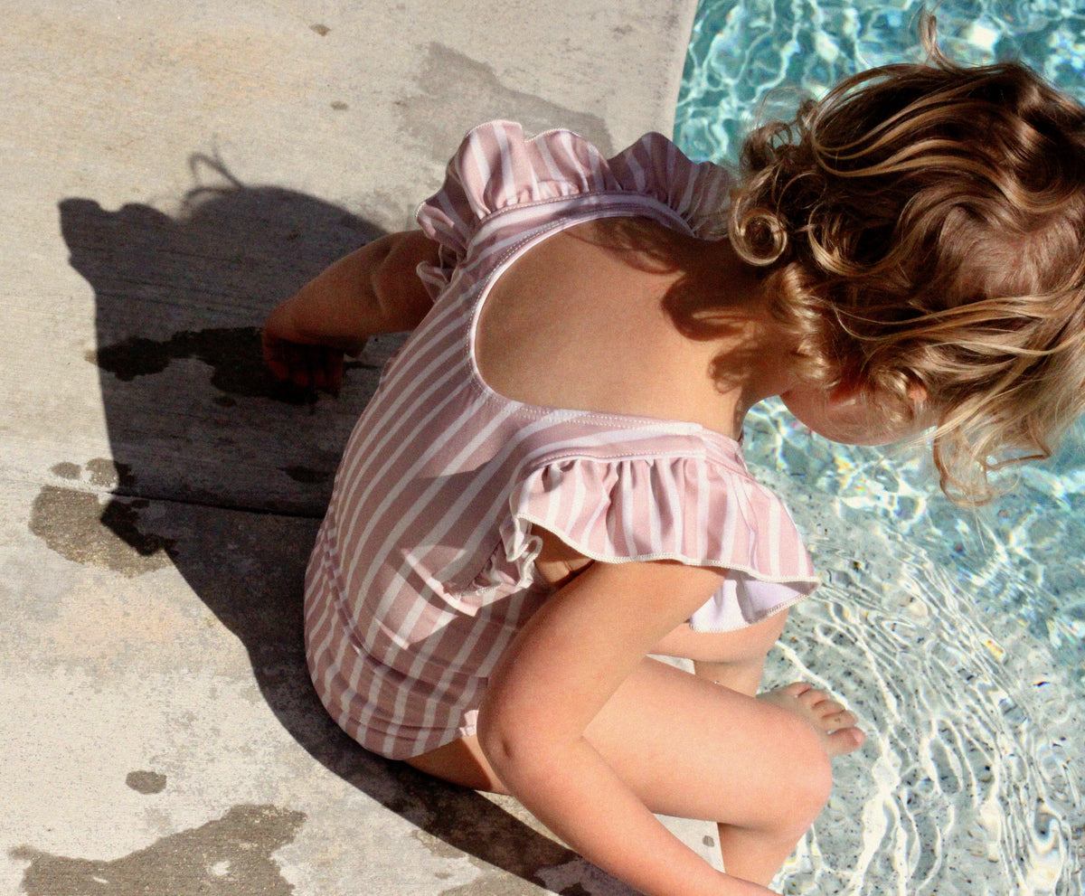 Girl sat on edge of pool in Pehr one-piece swim suit